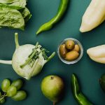A flat lay of fresh green vegetables and fruits on a green background, showcasing healthy eating.