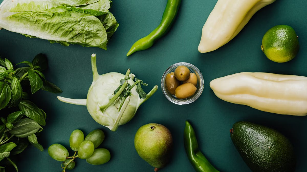 A flat lay of fresh green vegetables and fruits on a green background, showcasing healthy eating.